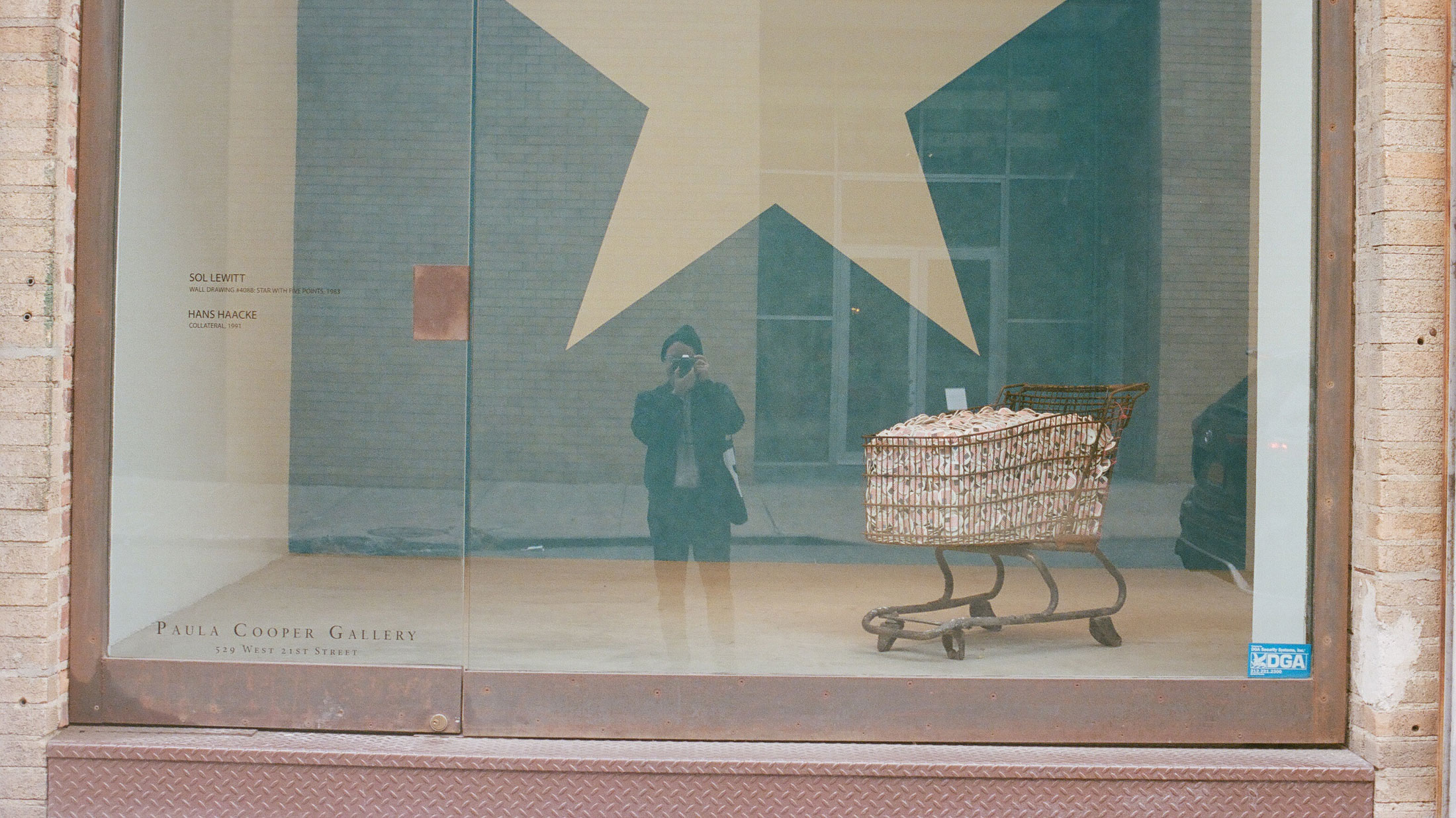 a photographer aims his camera at a reflective window, inside appears to be some modern art