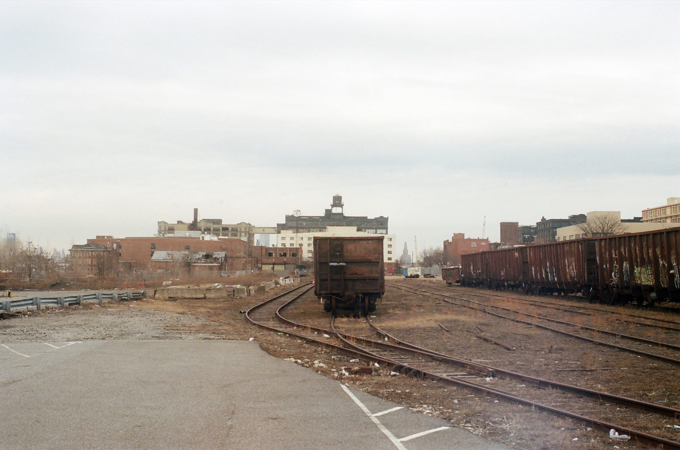 an abandoned train in a railyard with old buildings in the distant background