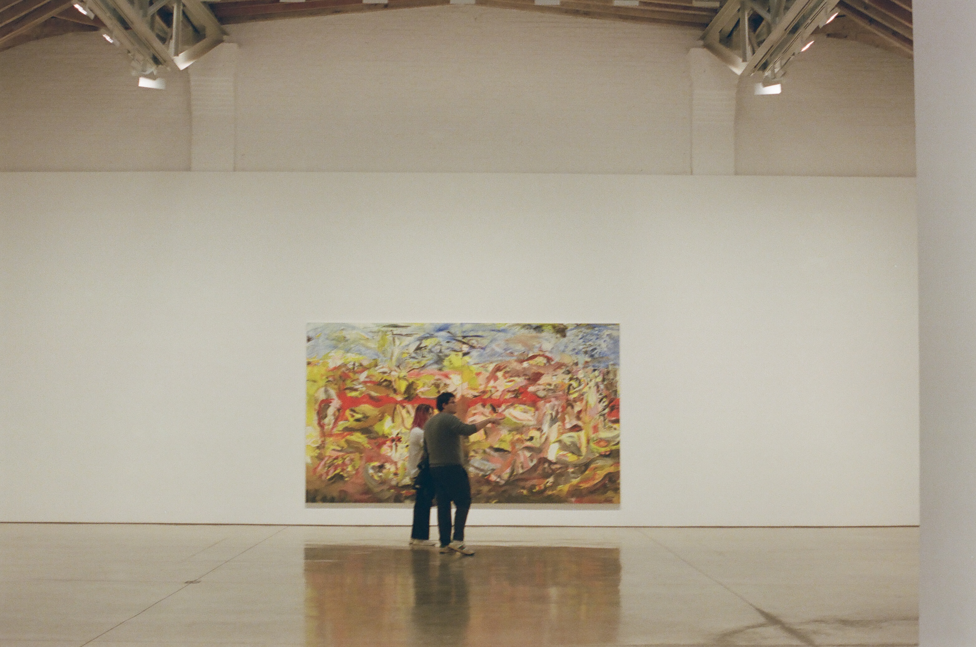 a blurry couple points around at the massive empty gallery with lofty ceilings in front of a beautiful, strange, and colorful painting