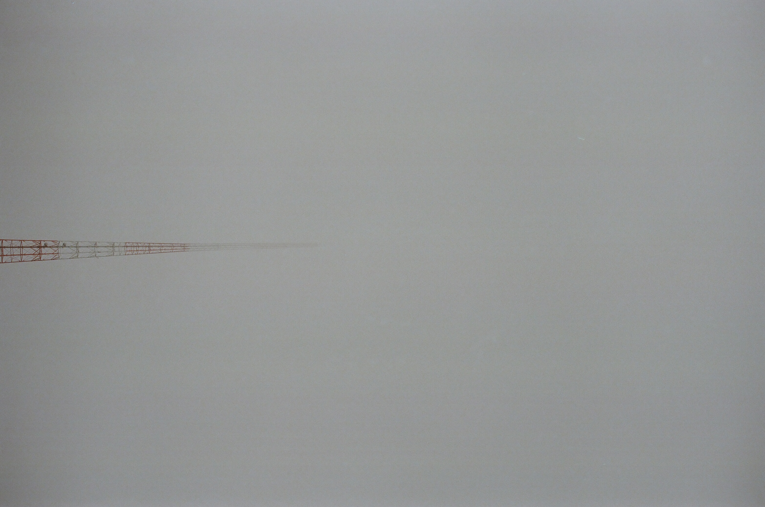 we are looking up at a very large but super skinny metal radiotower as it extends into the mysterious fog